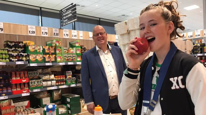 Kinderburgemeester Ayden snackt gezond en eet een appel. Op de achtergrond: wethouder Kees Weststrate.