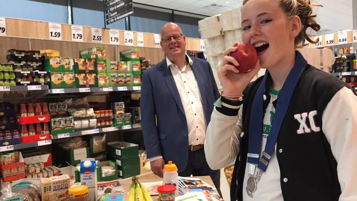 Kinderburgemeester Ayden snackt gezond en eet een appel. Op de achtergrond: wethouder Kees Weststrate.