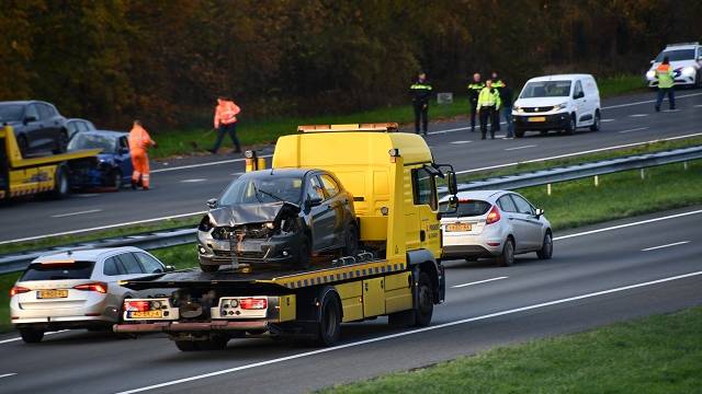 Bergers rijden de beschadigde auto's weg terwijl aan de andere kant de rijbaan wordt schoongemaakt