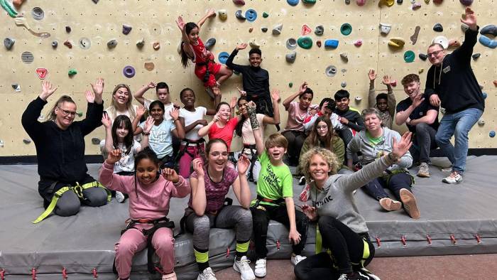 Groep juichende kinderen met begeleiders voor een klimmuur