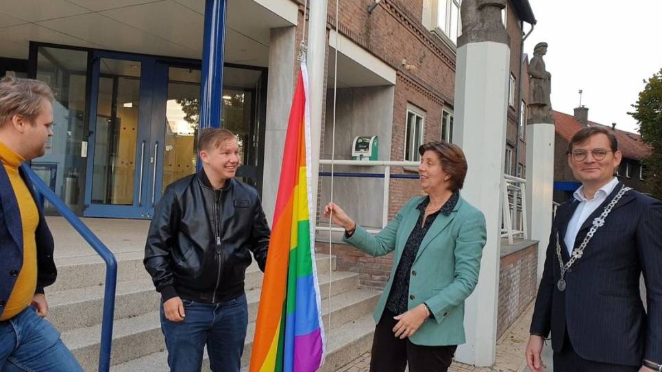 Wethouder Annebeth Evertz en inclusieambassadeur Maxim hijsen de Regenboogvlag tijdens Coming Out Day.