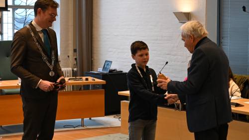 Oud-burgemeester Siebe Kramer (rechts) geeft de voorzittershamer aan kinderburgemeester Tygo. Links op de foto, burgemeester Constantijn Jansen op de Haar.