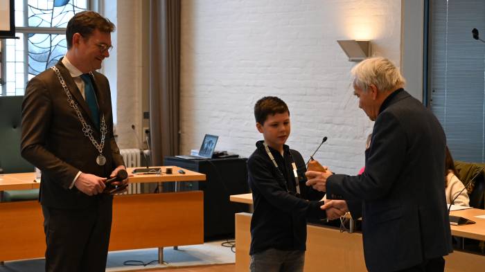 Oud-burgemeester Siebe Kramer (rechts) geeft de voorzittershamer aan kinderburgemeester Tygo. Links op de foto, burgemeester Constantijn Jansen op de Haar.